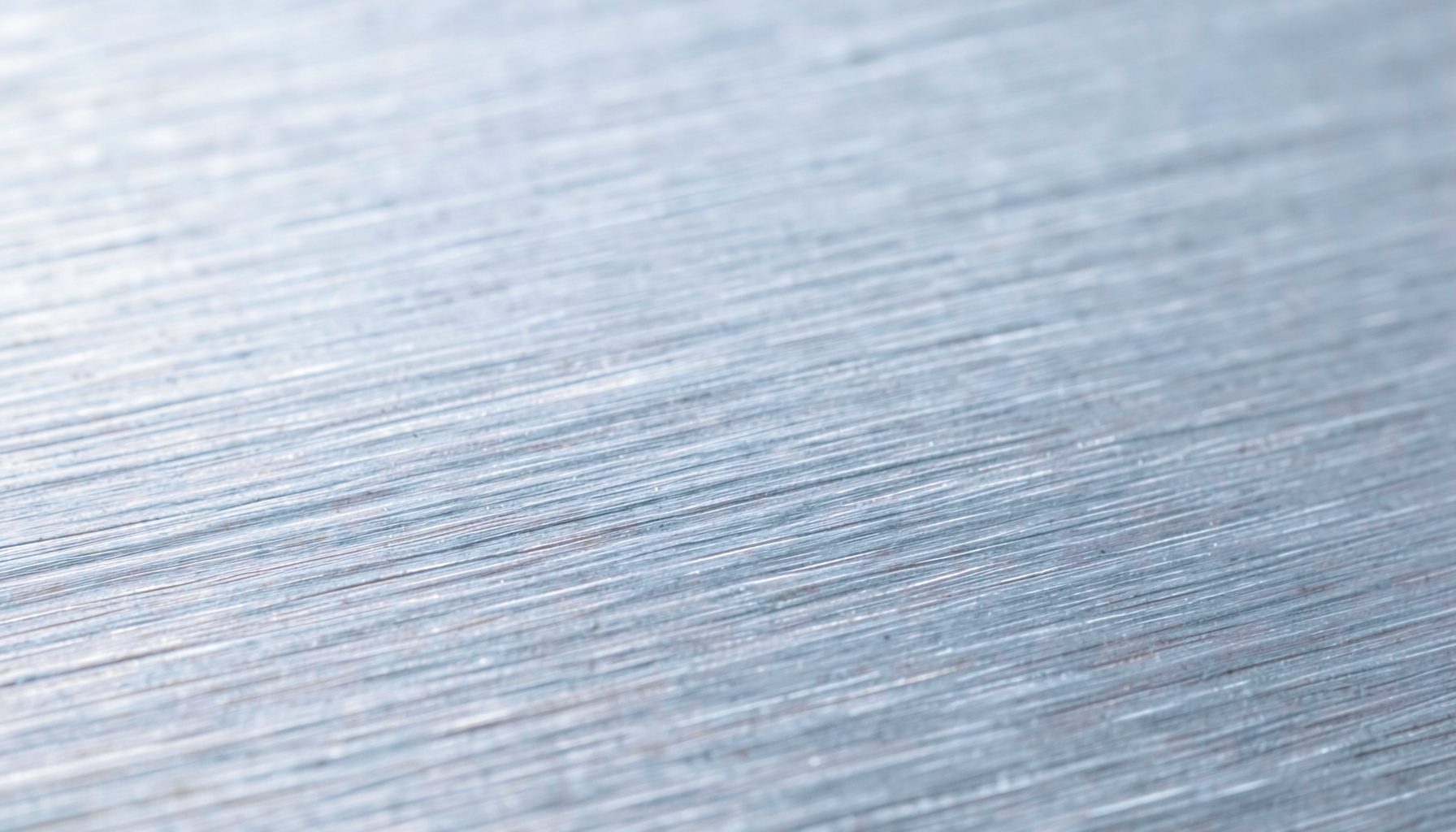 A close-up photograph of brushed stainless steel with fine horizontal grain lines, cool silver tones