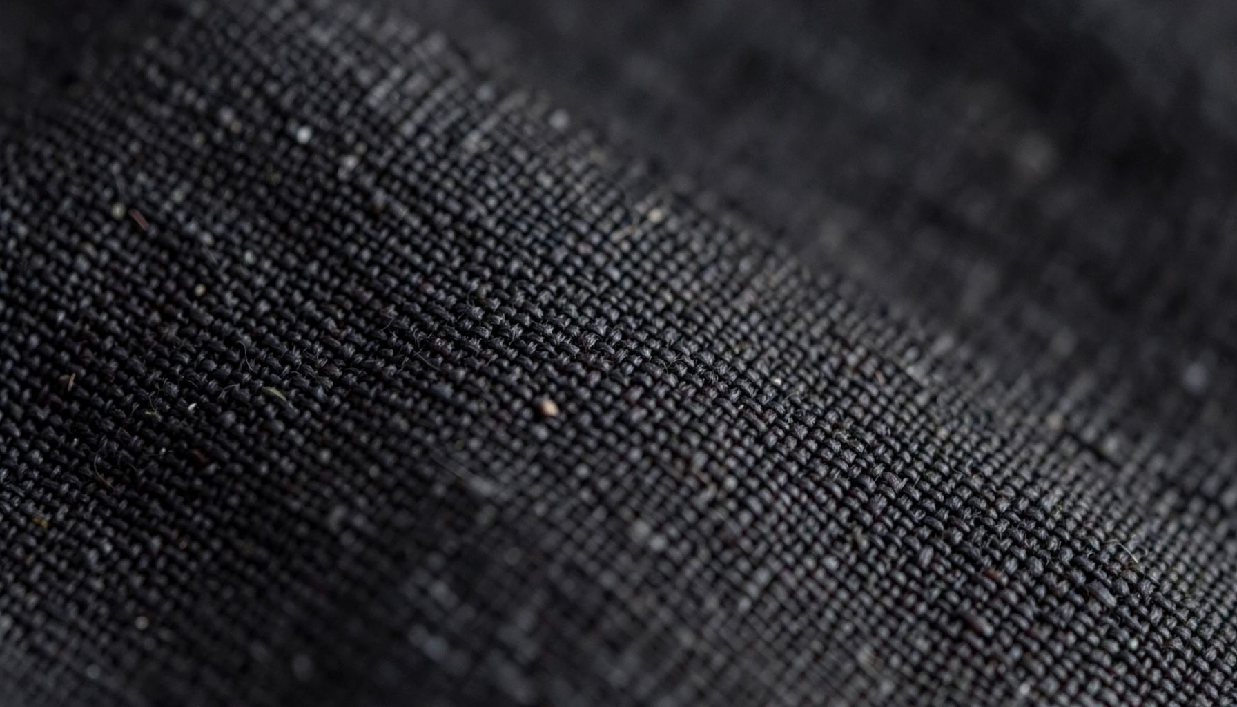A close-up photograph of textured linen fabric in deep charcoal, showing the weave pattern under soft light