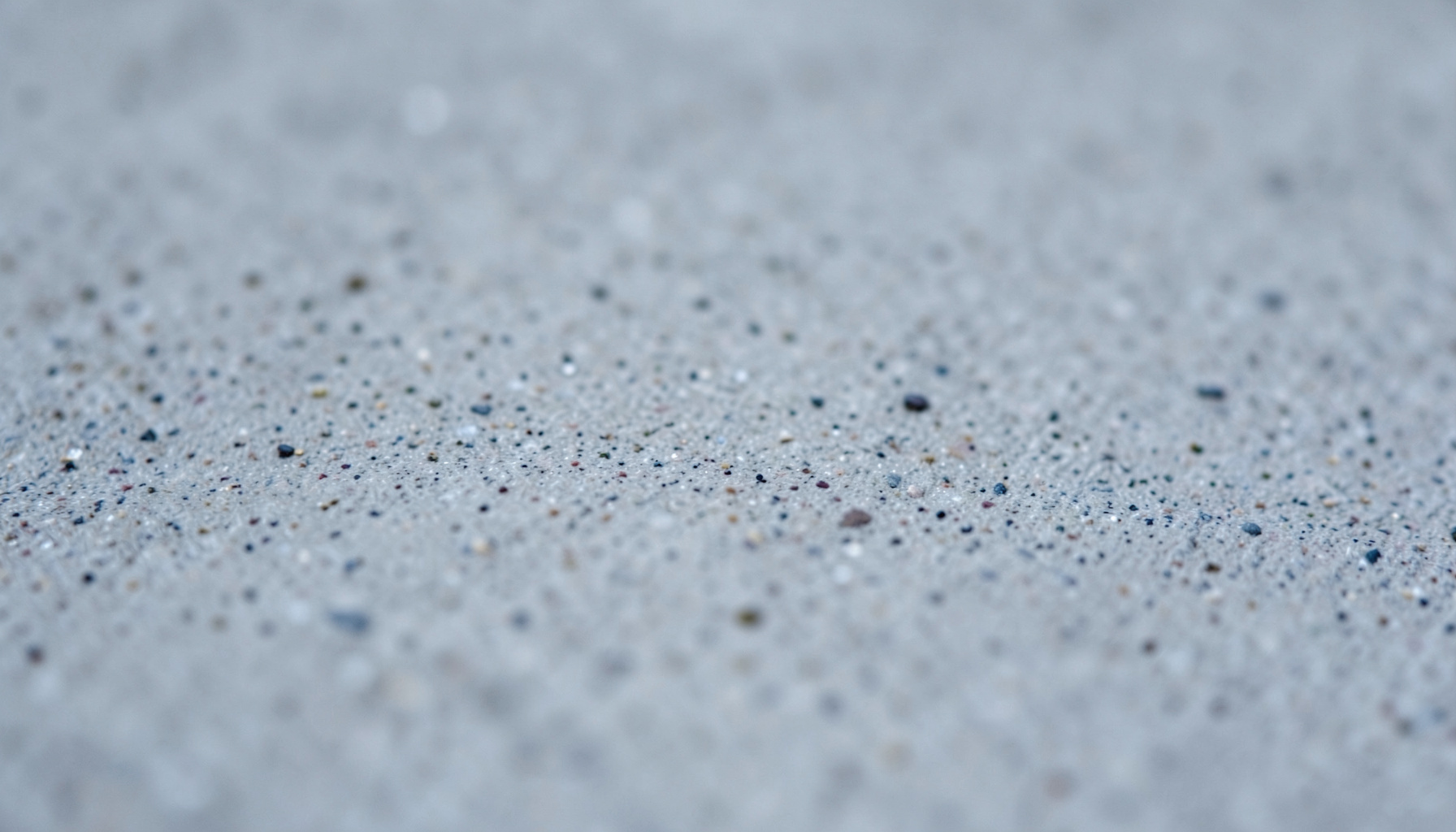 A close-up photograph of smooth concrete with faint aggregate speckles, cool gray tones