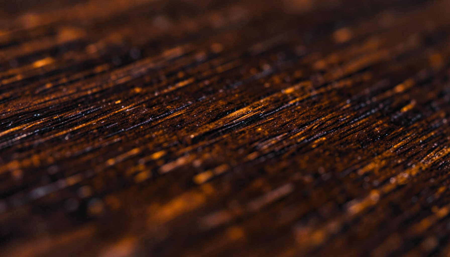 A close-up photograph of dark polished wood grain with subtle amber highlights, conveying warmth and craftsmanship