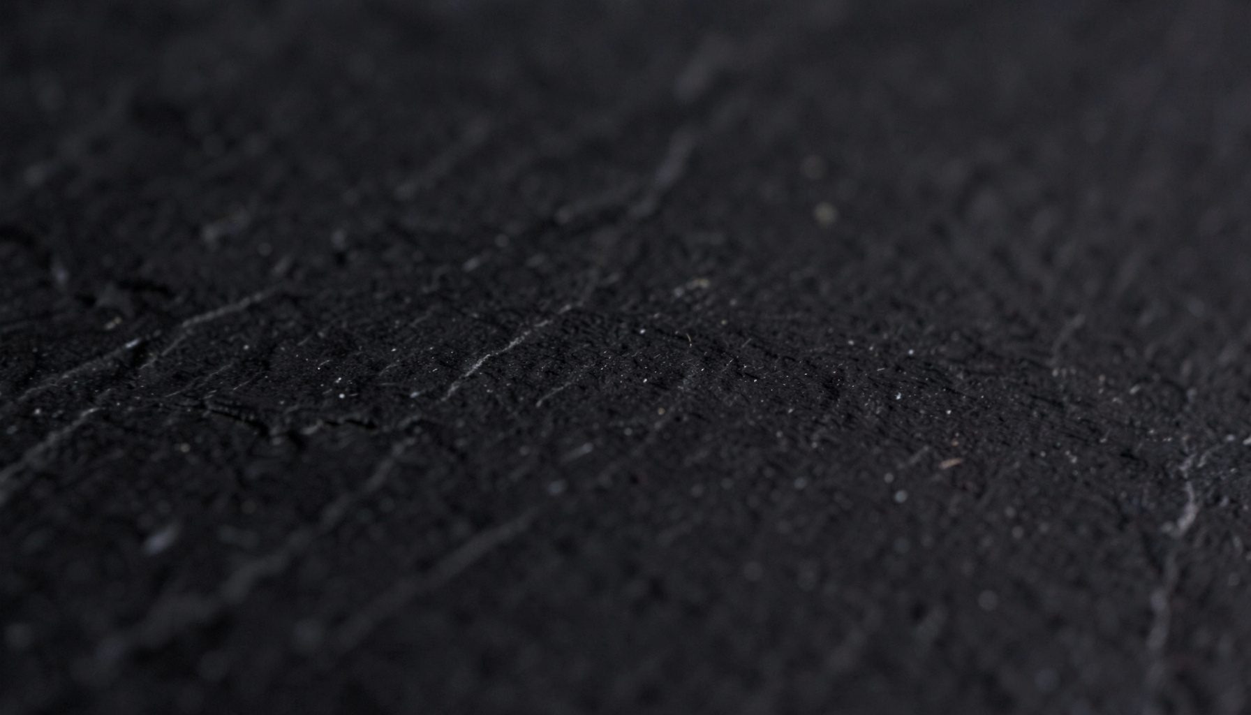 A close-up photograph of matte black slate with faint natural striations, deep charcoal tones