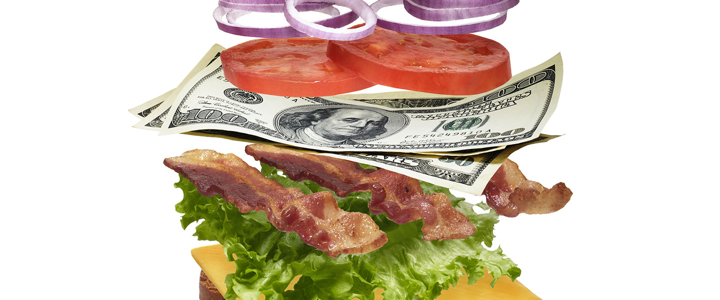A stacked sandwich with lettuce, bacon, cheese, tomato, and onion, rich reds and golden browns against a dark backdrop