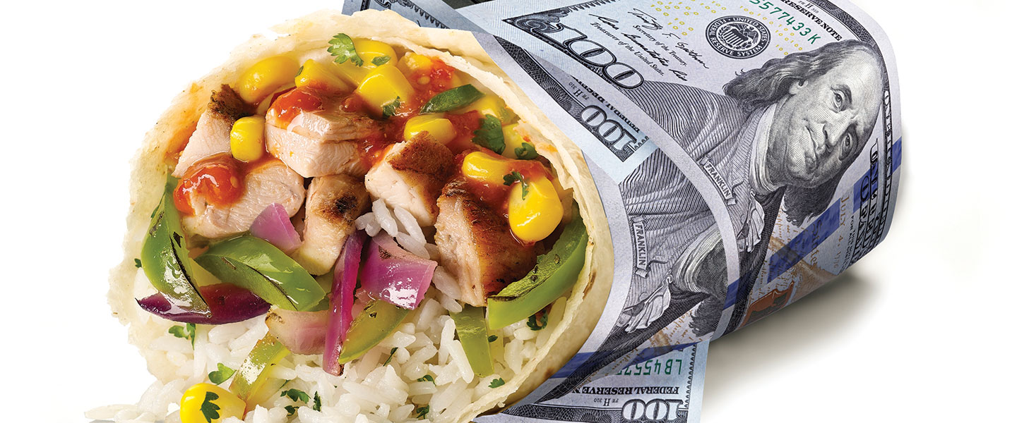 A wrapped burrito filled with grilled chicken, rice, corn, peppers and onion, partially wrapped in a large denomination bill, on a dark surface